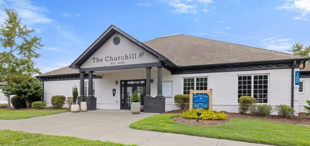 outdoor view of leasing office with welcome sign, landscaping, and sidewalk