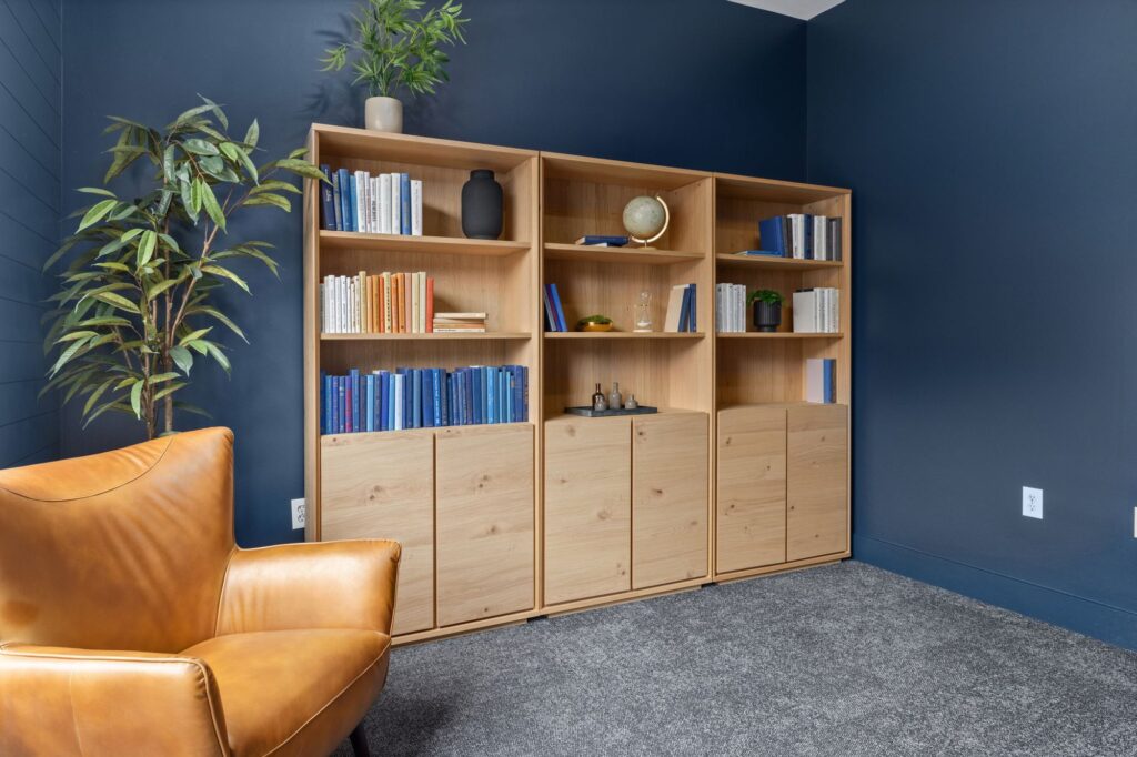 bookshelves lining a wall in a room with a leather lounge chair in the corner and various plant decor
