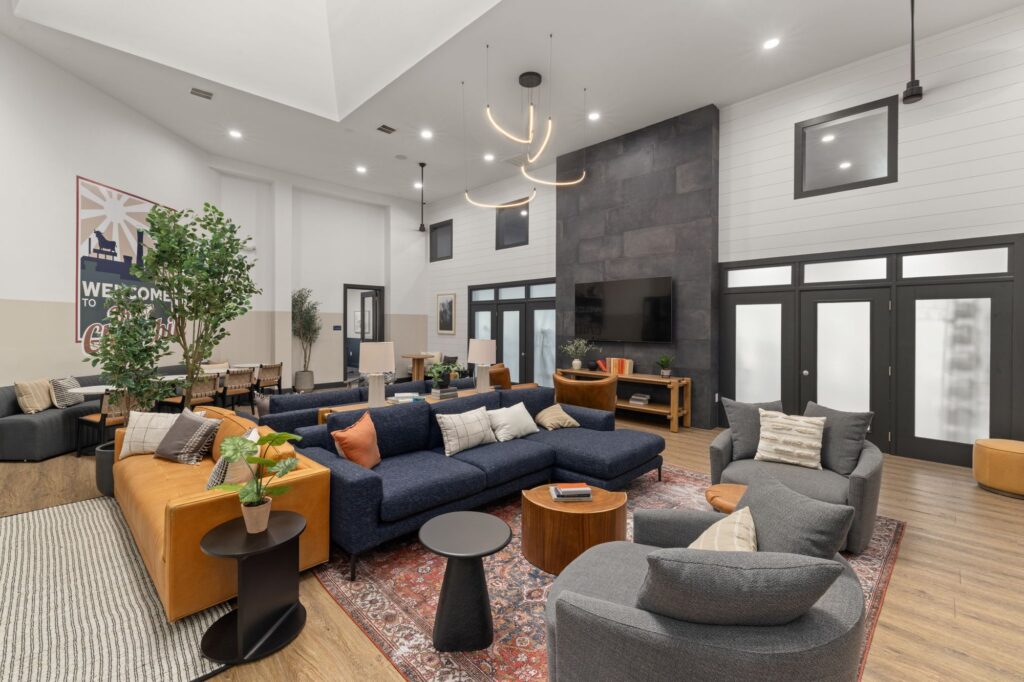 Clubhouse lounge with sofa and lounge chairs, mounted television, coffee tables and chandelier lighting