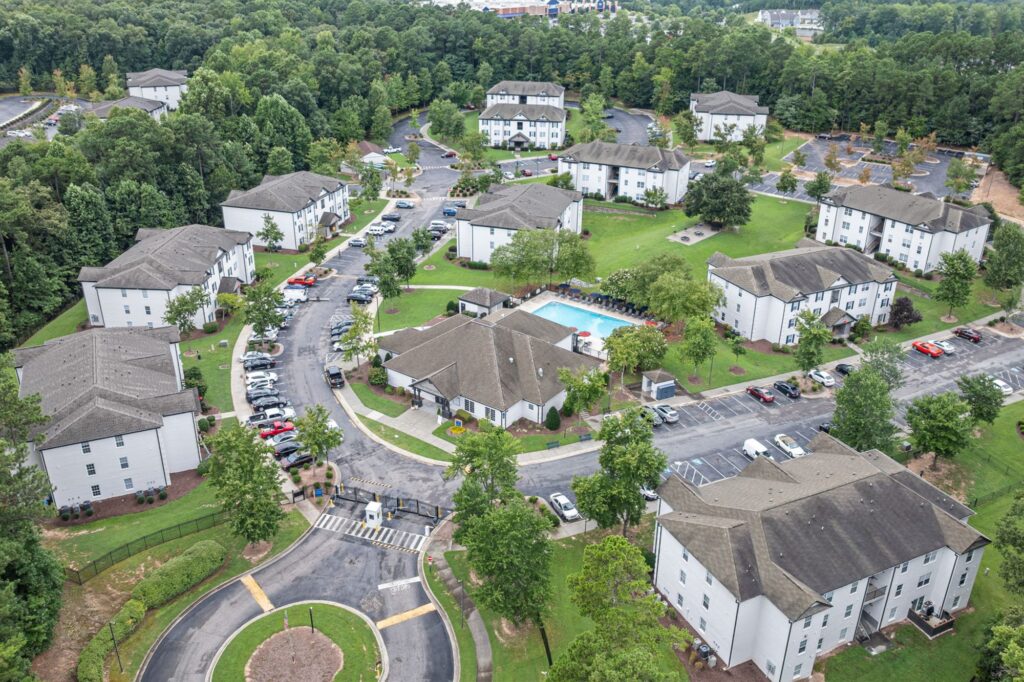 Outside aerial view of apartment buildings, central leasing office, landscaping and parking